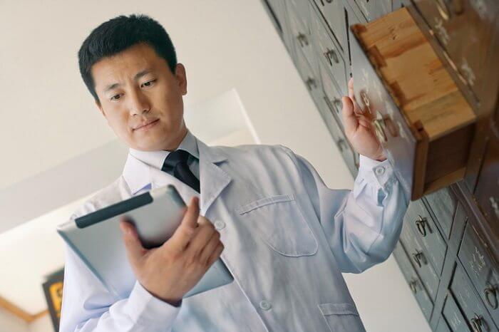 Chinese doctor with tablet looking through old library