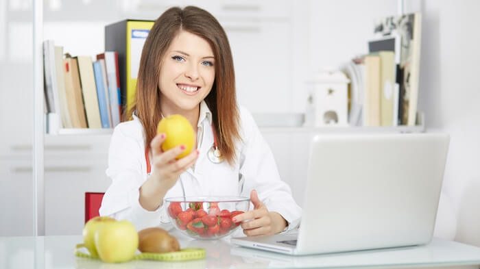 bio individuality concept - nutritionist with fruit on desk holding apple
