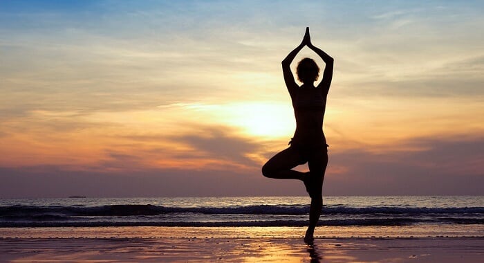 holistic health concept - woman doing yoga on beach at dusk