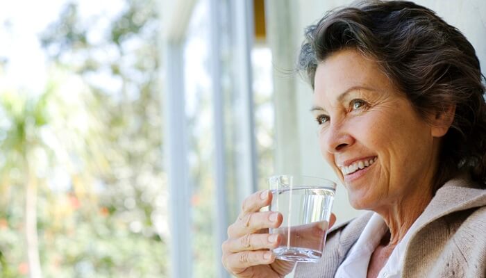senior woman holding glass of water - holistic health tips concept