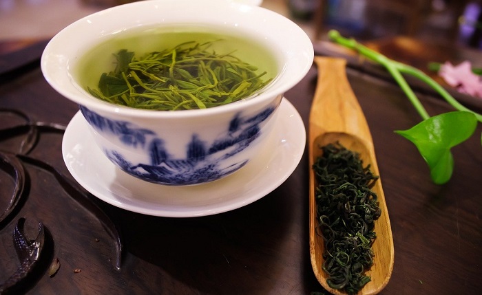 cup of green tea and green tea leaves in wooden spoon